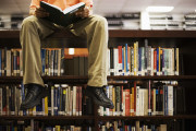 Man Reading Book and Sitting on Bookshelf in Library
